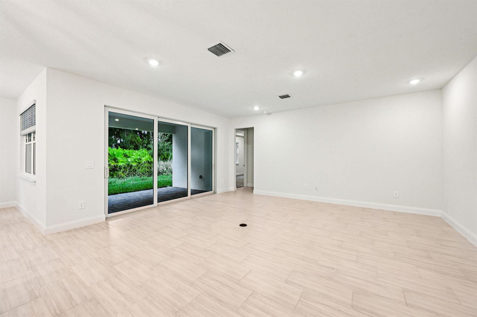 An empty living room features light wood-look tile floors, white walls, and large sliding glass doors — 5625 Hampton Park Circle, Vero Beach FL 32966, VERO BEACH, FL
