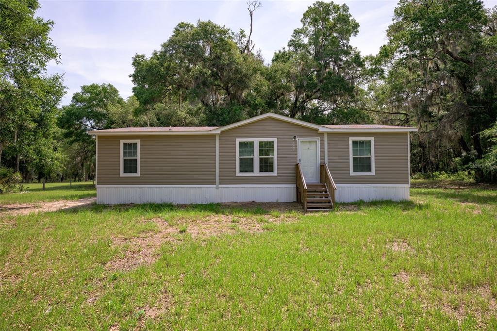 A single-story manufactured home with tan siding sits on a grassy lot with trees — 374 SISCO ROAD, POMONA PARK, FL