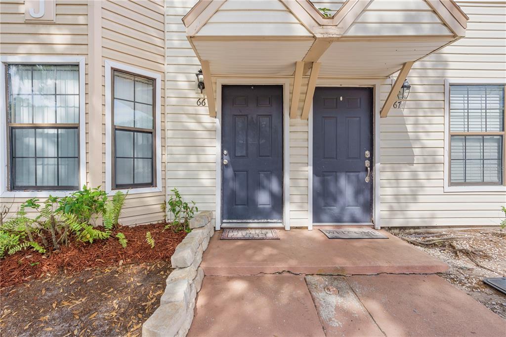 The exterior of a residential building shows two dark blue front doors labeled 66 and 67 — 2302 MAKI ROAD UNIT 66, PLANT CITY, FL