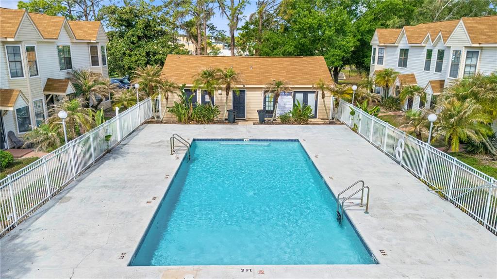 An outdoor swimming pool is surrounded by a concrete deck, white fencing, and apartment buildings — 2302 MAKI ROAD UNIT 66, PLANT CITY, FL