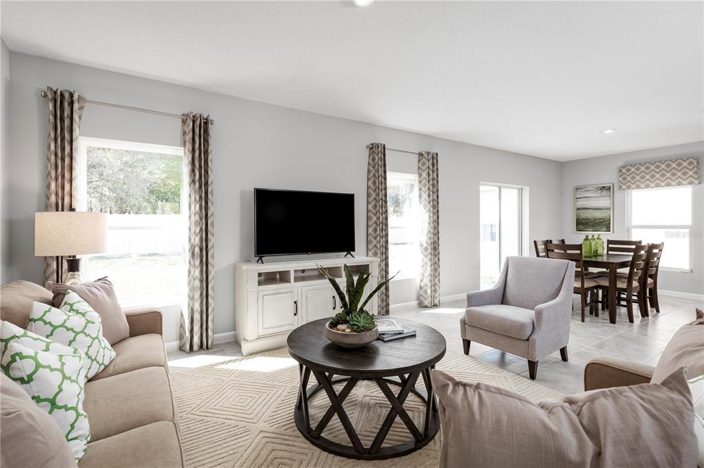 A bright living room features a television, coffee table, armchairs, and an adjacent dining area — 6938 SUNDIAL DRIVE, LAKELAND, FL