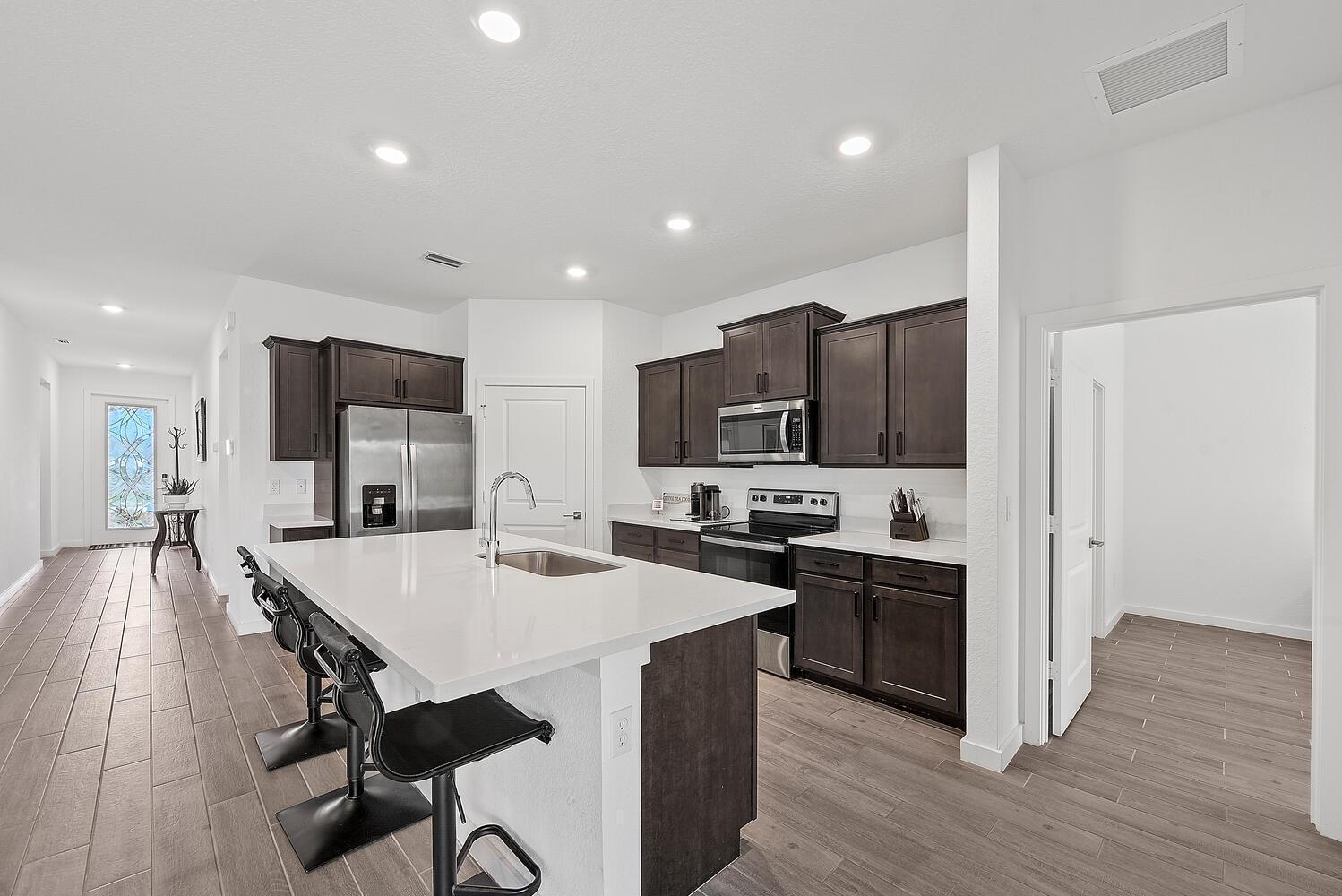 A kitchen with dark wood cabinets, white countertops, a central island, and wood-look tile flooring — 4444 NW King Court, Jensen Beach FL 34957, JENSEN BEACH, FL