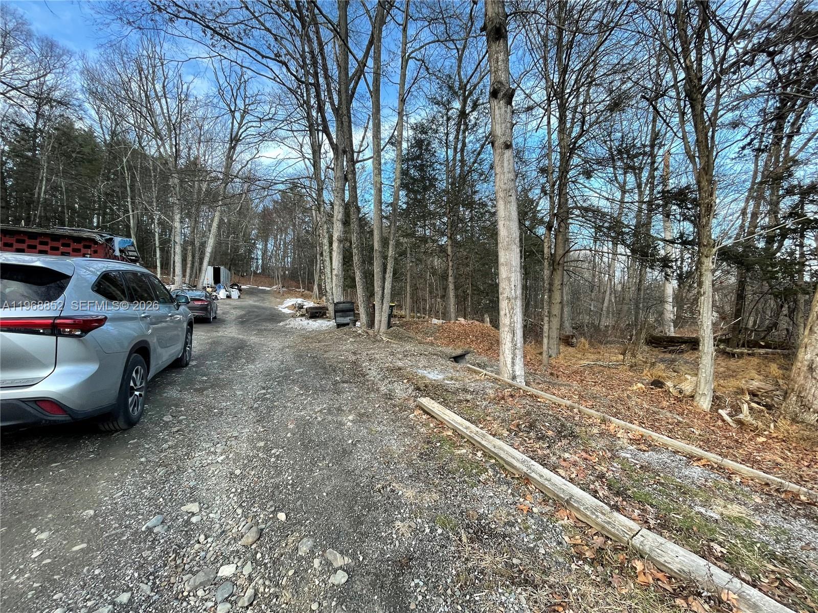 A gravel driveway leads past a parked car toward a wooded area with bare trees — 34 Iken Road, NY 12446, NY
