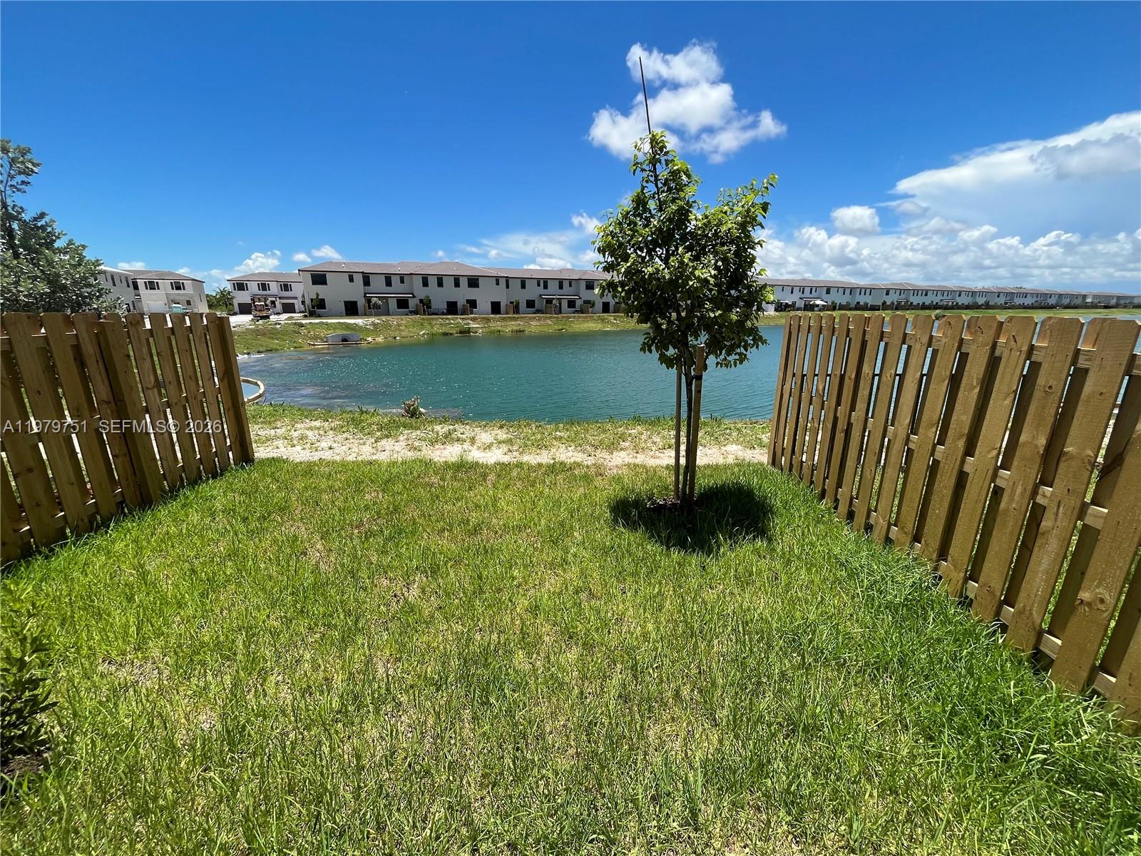 A grassy backyard features a small tree and a wooden fence overlooking a pond — 9960 SW 228th Ter, Miami FL 33190, MIAMI, FL