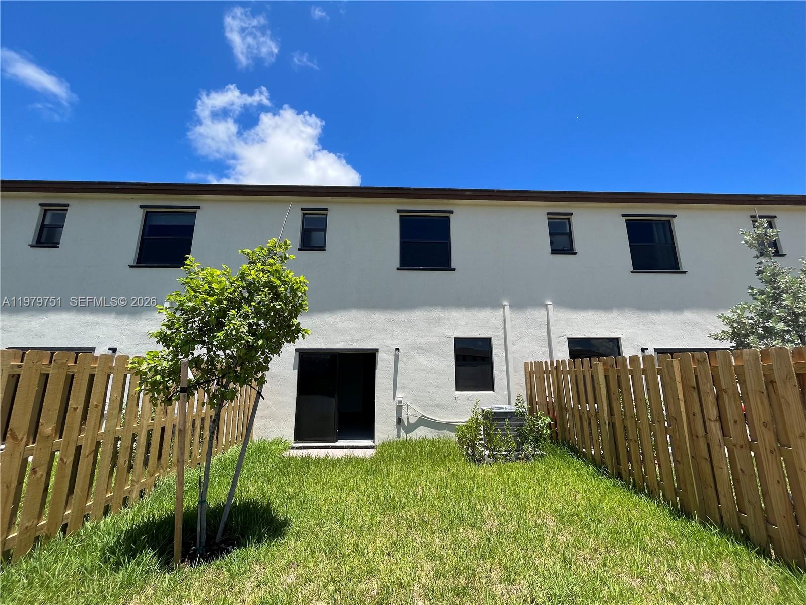The exterior of a two-story townhouse features a small backyard with a wooden fence — 9960 SW 228th Ter, Miami FL 33190, MIAMI, FL