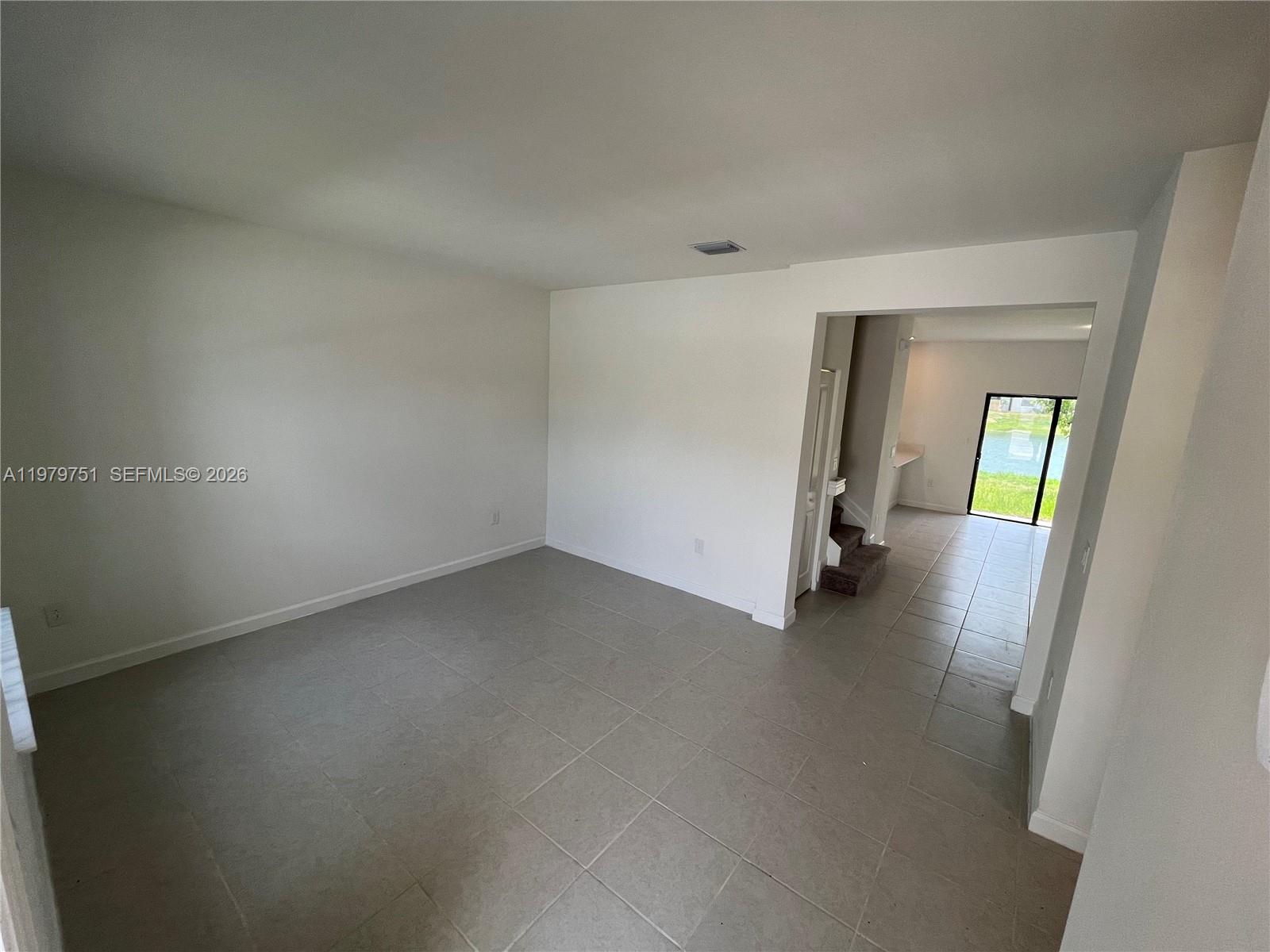 An empty room with light-colored tile flooring leads to a doorway with a water view — 9960 SW 228th Ter, Miami FL 33190, MIAMI, FL