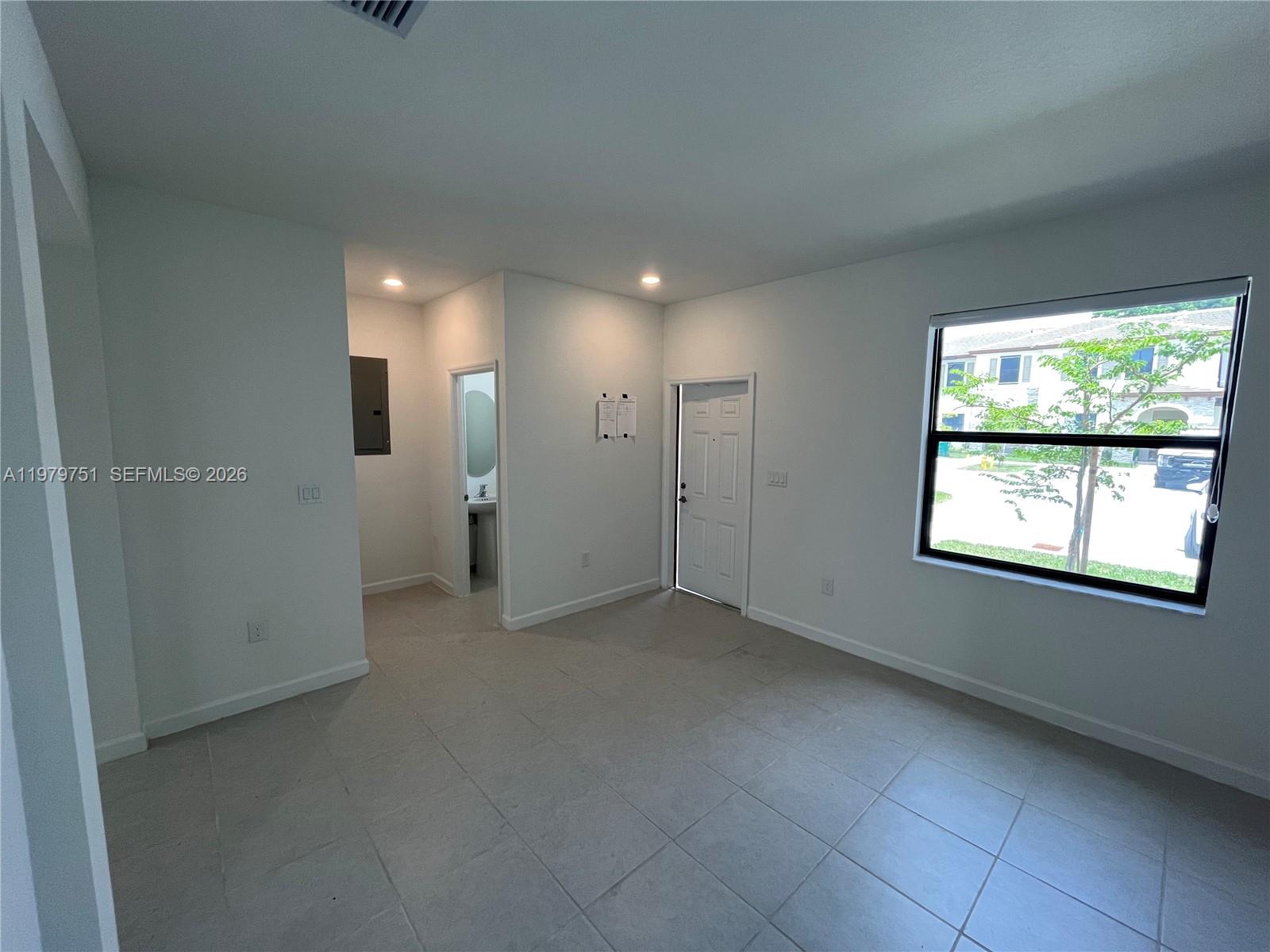 An empty room with light tile flooring, white walls, a window, and a doorway — 9960 SW 228th Ter, Miami FL 33190, MIAMI, FL
