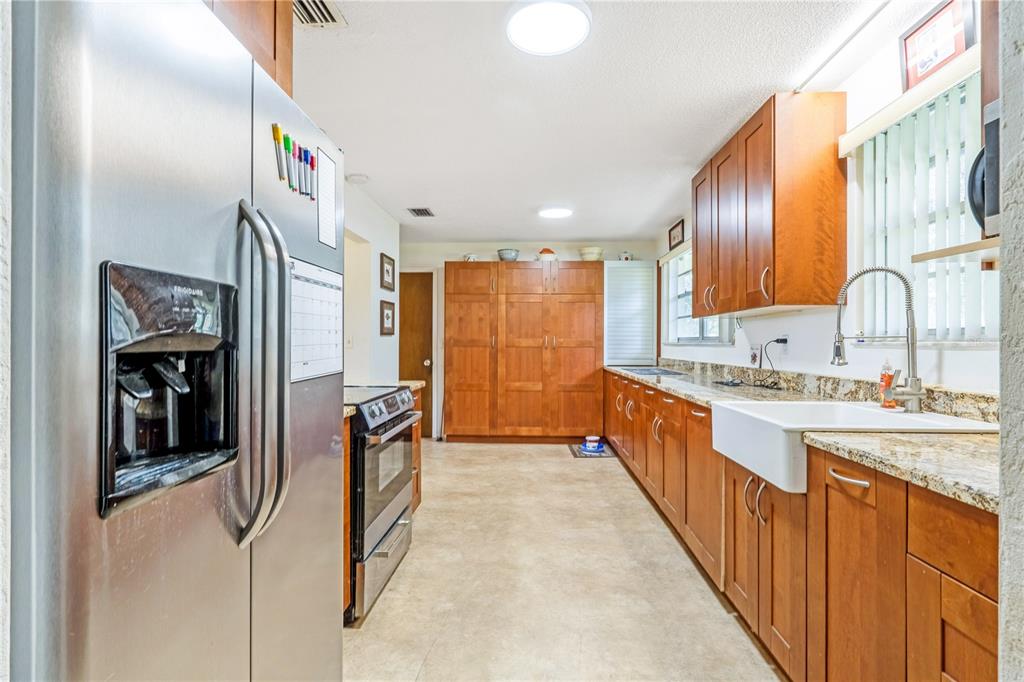 A kitchen with wood cabinets, granite countertops, a farmhouse sink, and stainless steel appliances — 24 OAK STREET, PORT ORANGE, FL