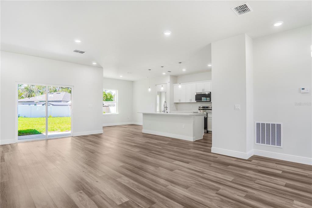 An open-concept kitchen and living area with wood-look flooring and a sliding glass door — 3908 SW 171ST LANE, OCALA, FL