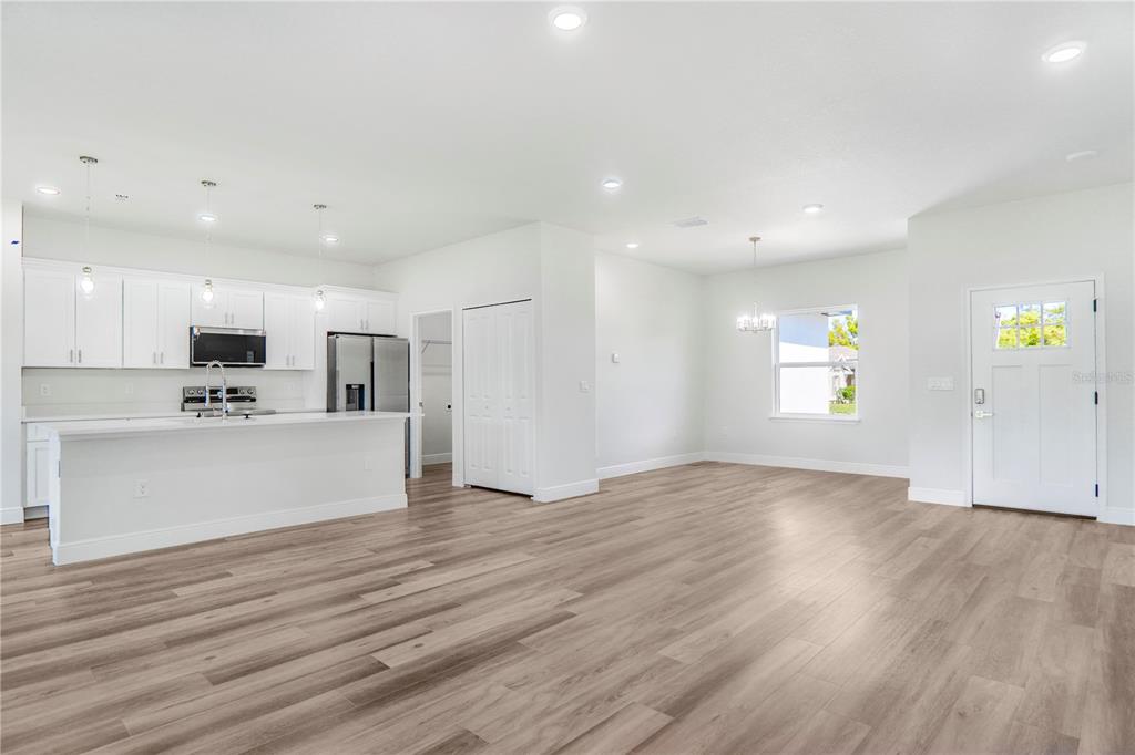 An open-concept kitchen and living area featuring white cabinets, stainless appliances, and wood-look flooring — 3908 SW 171ST LANE, OCALA, FL
