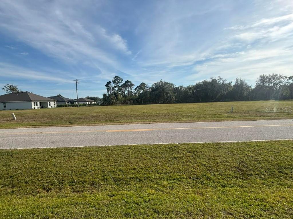 A vacant, grassy lot sits across a paved road from a residential neighborhood — 25261 DOREDO DRIVE, PUNTA GORDA, FL