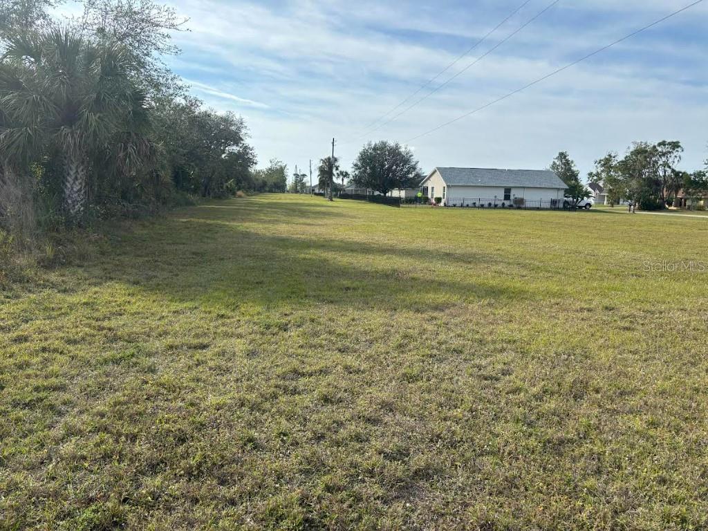 A large, flat, grassy vacant lot stretches toward a house in the distance — 25261 DOREDO DRIVE, PUNTA GORDA, FL