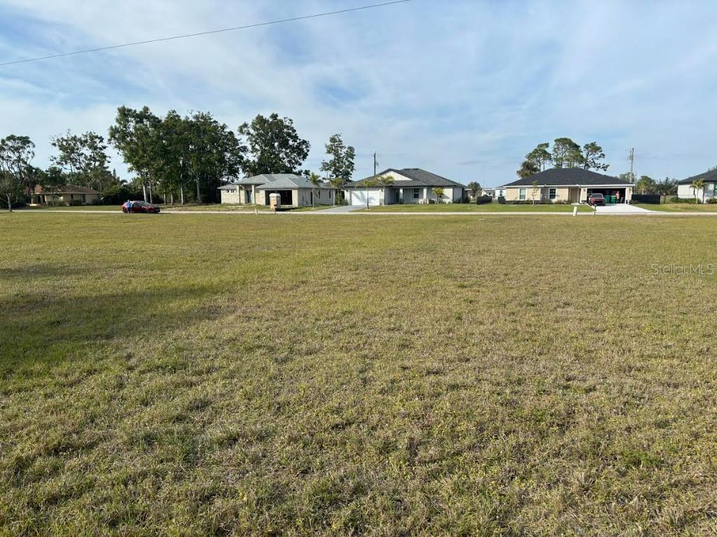 A large, vacant grassy lot sits in front of several suburban single-family homes — 25261 DOREDO DRIVE, PUNTA GORDA, FL
