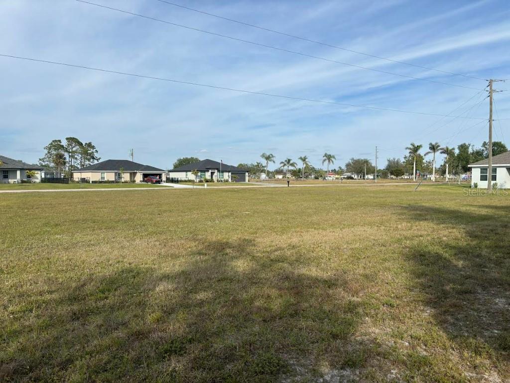 A wide, grassy vacant lot sits in front of several suburban houses under a blue sky — 25261 DOREDO DRIVE, PUNTA GORDA, FL