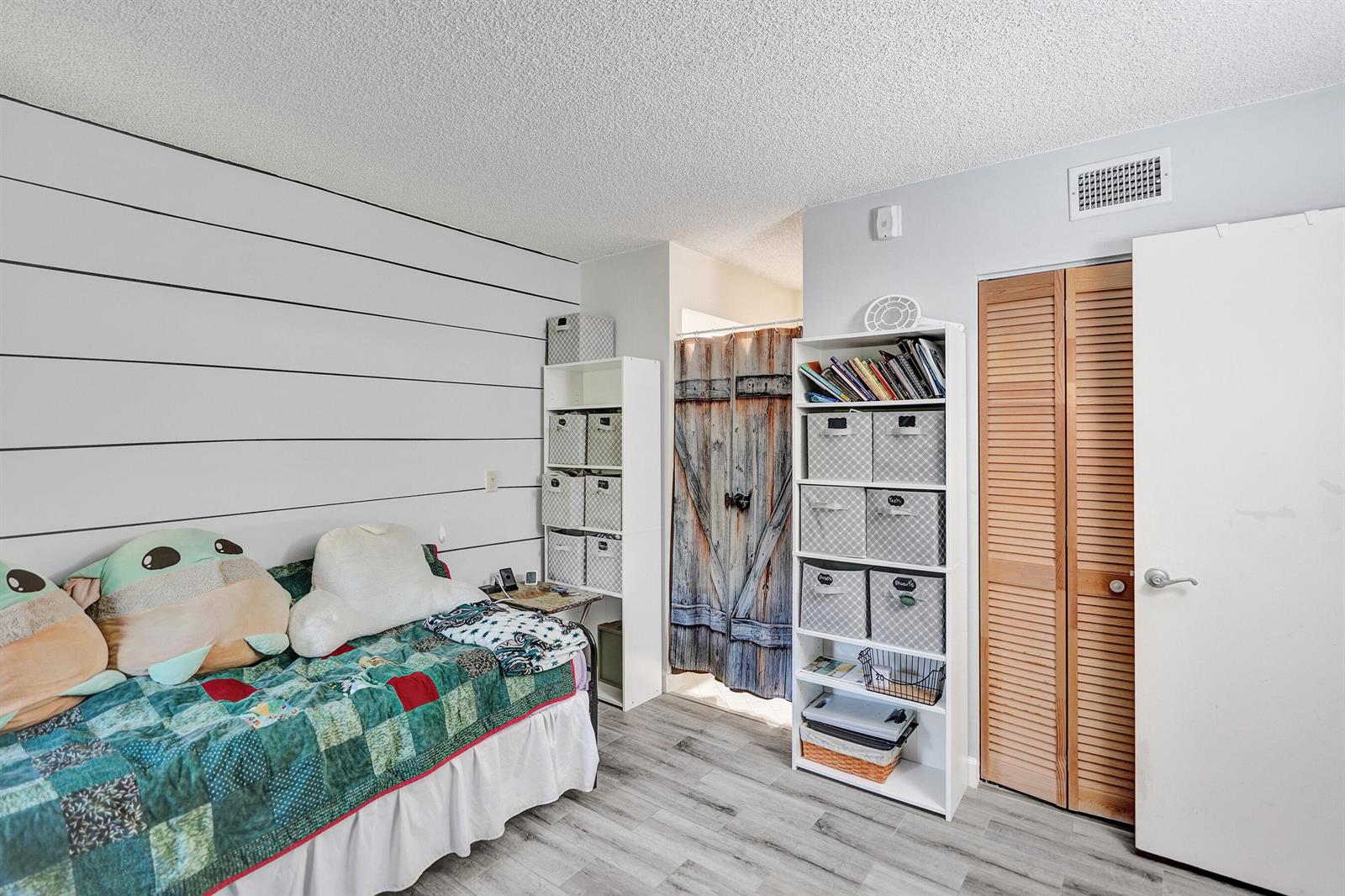 A bedroom features a twin bed, two white shelving units, and a wood-look door — 5201 W Club Circle # 103, Boca Raton FL 33431, BOCA RATON, FL
