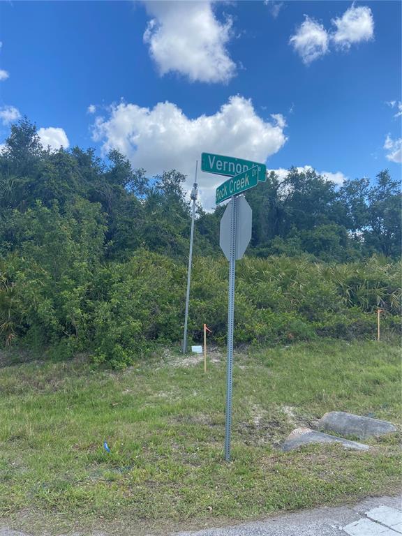 A street sign for Vernon Drive and Rock Creek Drive stands in a grassy, wooded area — 1190 VERNON AVE, PORT CHARLOTTE, FL