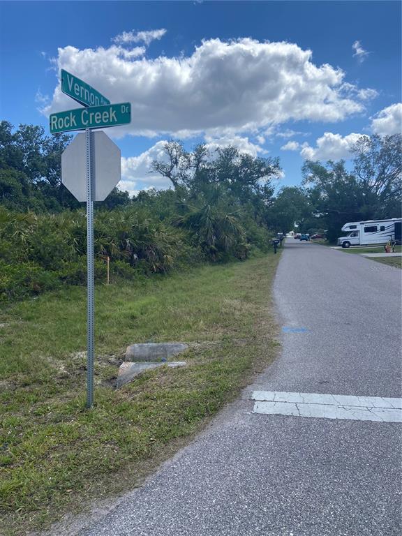 A street sign for Vernon Ave and Rock Creek Dr stands beside a paved road — 1190 VERNON AVE, PORT CHARLOTTE, FL