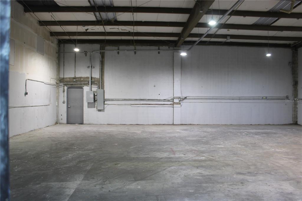 An empty warehouse interior features concrete floors, white walls, exposed ceiling beams, and a metal door — 977 WITHLACOOCHEE STREET UNIT D, SAFETY HARBOR, FL