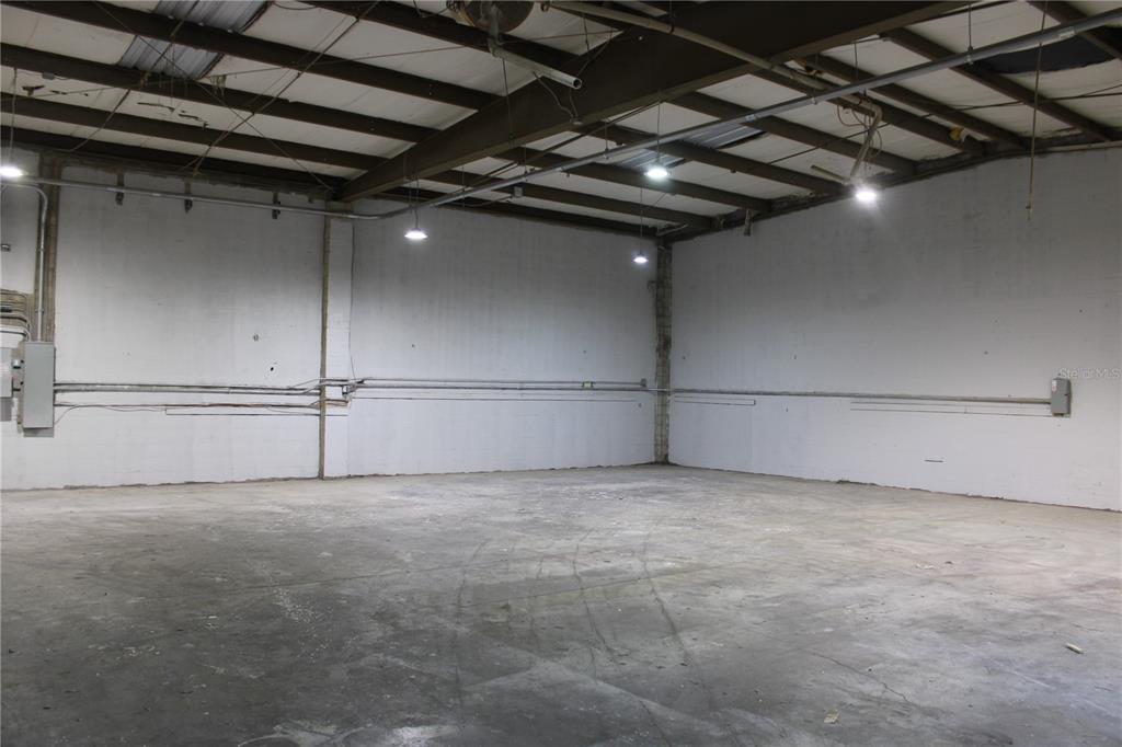 An empty warehouse space features white concrete walls, exposed ceiling beams, and overhead lighting — 977 WITHLACOOCHEE STREET UNIT D, SAFETY HARBOR, FL