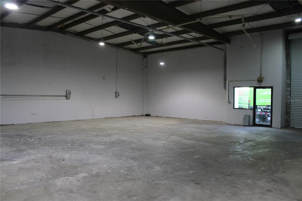 An empty warehouse space features concrete floors, white walls, exposed ceiling beams, and a glass door — 977 WITHLACOOCHEE STREET UNIT D, SAFETY HARBOR, FL