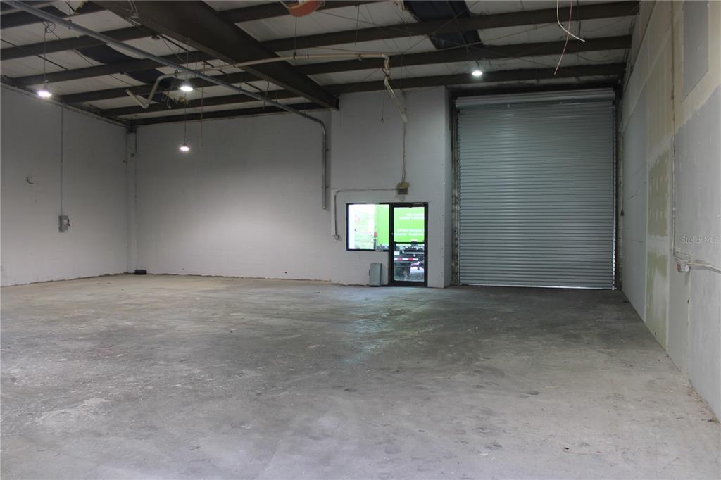 An empty industrial warehouse space features a concrete floor, white walls, and a roll-up door — 977 WITHLACOOCHEE STREET UNIT D, SAFETY HARBOR, FL