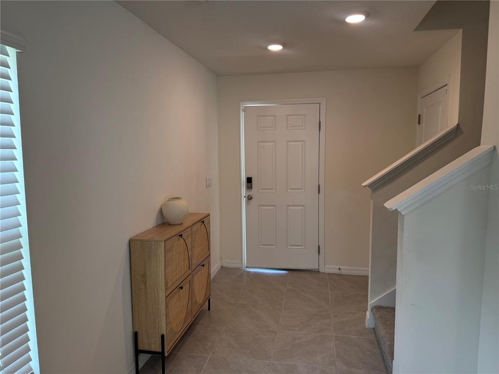 An entryway features a white front door, tile flooring, a wooden cabinet, and a staircase — 8594 SW 46TH AVENUE, OCALA, FL