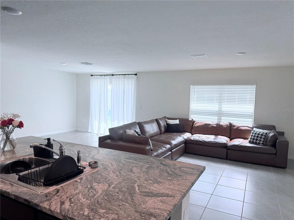 A kitchen island with a granite countertop overlooks a living room with a brown sectional — 8594 SW 46TH AVENUE, OCALA, FL