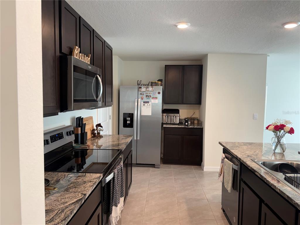 A kitchen features dark wood cabinets, granite countertops, stainless steel appliances, and tile flooring — 8594 SW 46TH AVENUE, OCALA, FL