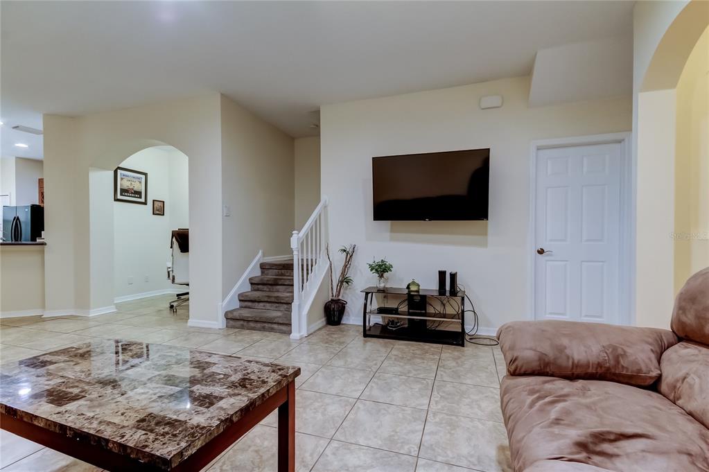 A living room features tile flooring, a wall-mounted television, and stairs leading to an upper level — 12660 SILVERDALE STREET, TAMPA, FL