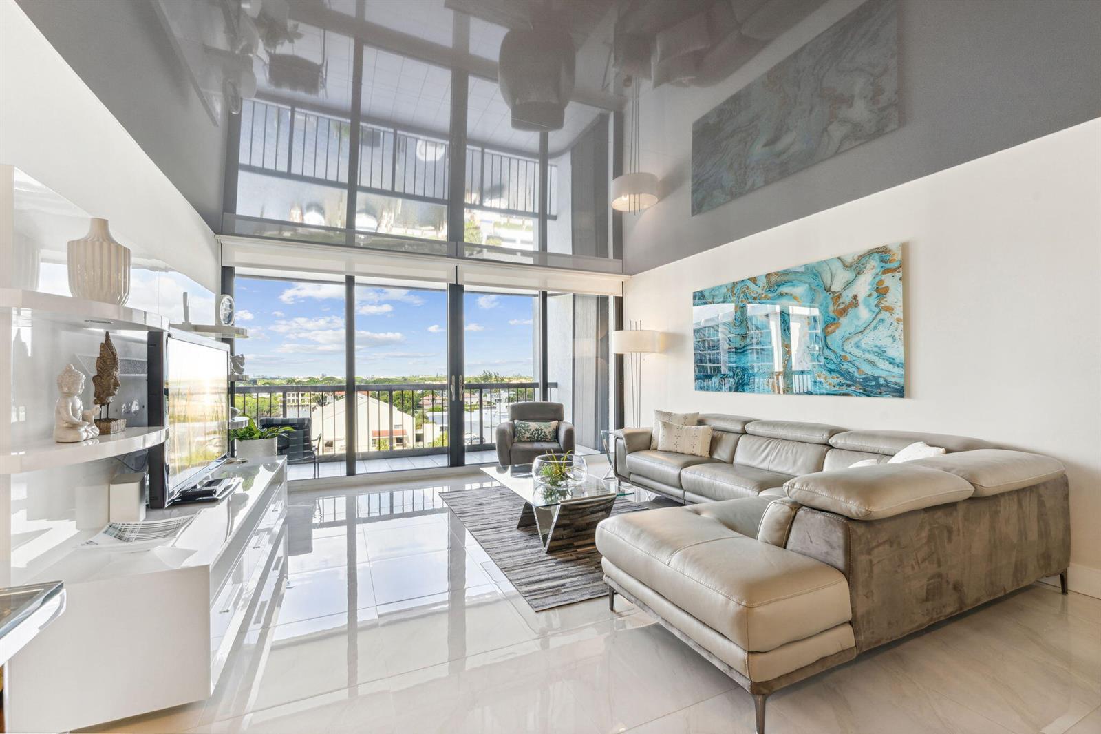 A modern living room features a high-gloss ceiling, floor-to-ceiling windows, and a large sectional sofa — 4748 S Ocean Boulevard # 806, Highland Beach FL 33487, HIGHLAND BEACH, FL