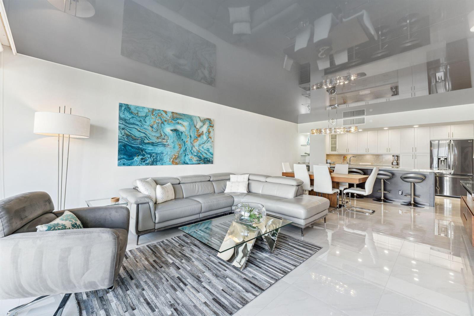 A modern open-concept living and dining area features a grey sectional, glass table, and kitchen — 4748 S Ocean Boulevard # 806, Highland Beach FL 33487, HIGHLAND BEACH, FL