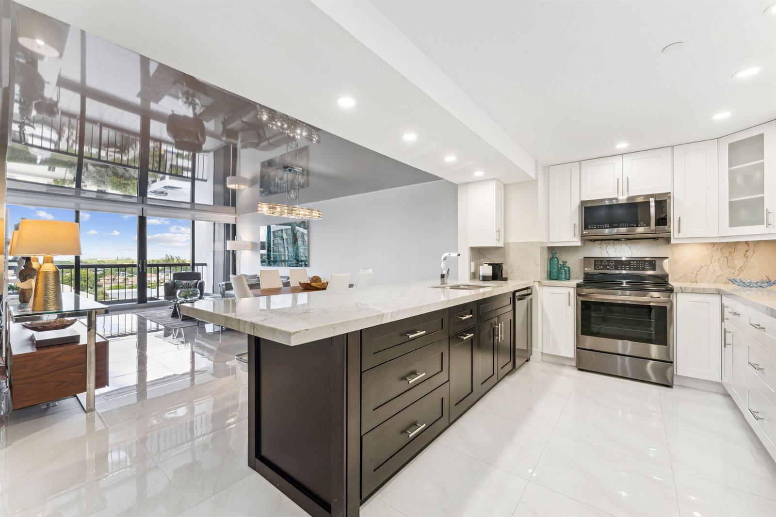 A modern kitchen with dark cabinetry and a white marble island overlooks a living area — 4748 S Ocean Boulevard # 806, Highland Beach FL 33487, HIGHLAND BEACH, FL