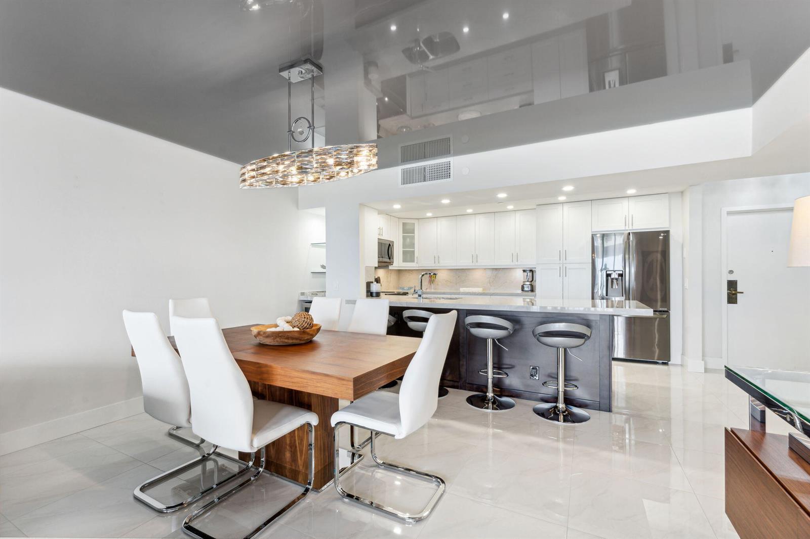A modern dining area with a wooden table and white chairs sits before an open kitchen — 4748 S Ocean Boulevard # 806, Highland Beach FL 33487, HIGHLAND BEACH, FL