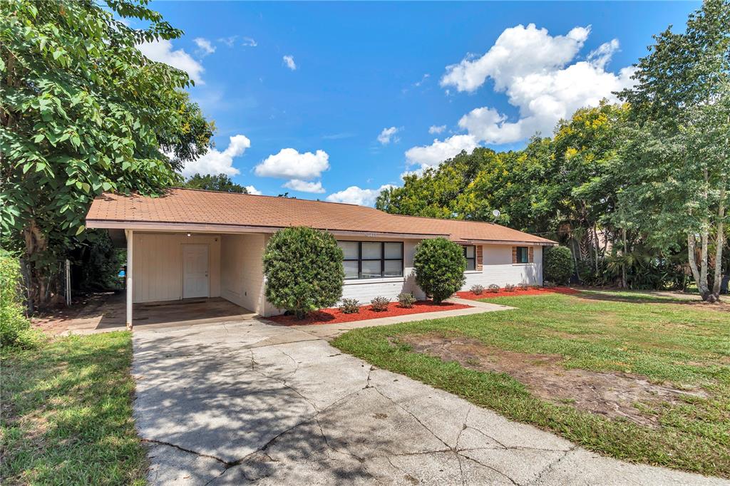 A single-story house with a carport, a concrete driveway, and a front lawn under trees — 2433 NE 2ND STREET, OCALA, FL