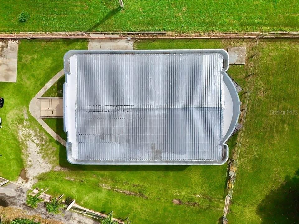 An aerial view shows a rectangular building with a metal roof and surrounding grassy yard — Carr. 760 KM 0.4 BO. EMAJAGUAS, MAUNABO, PR