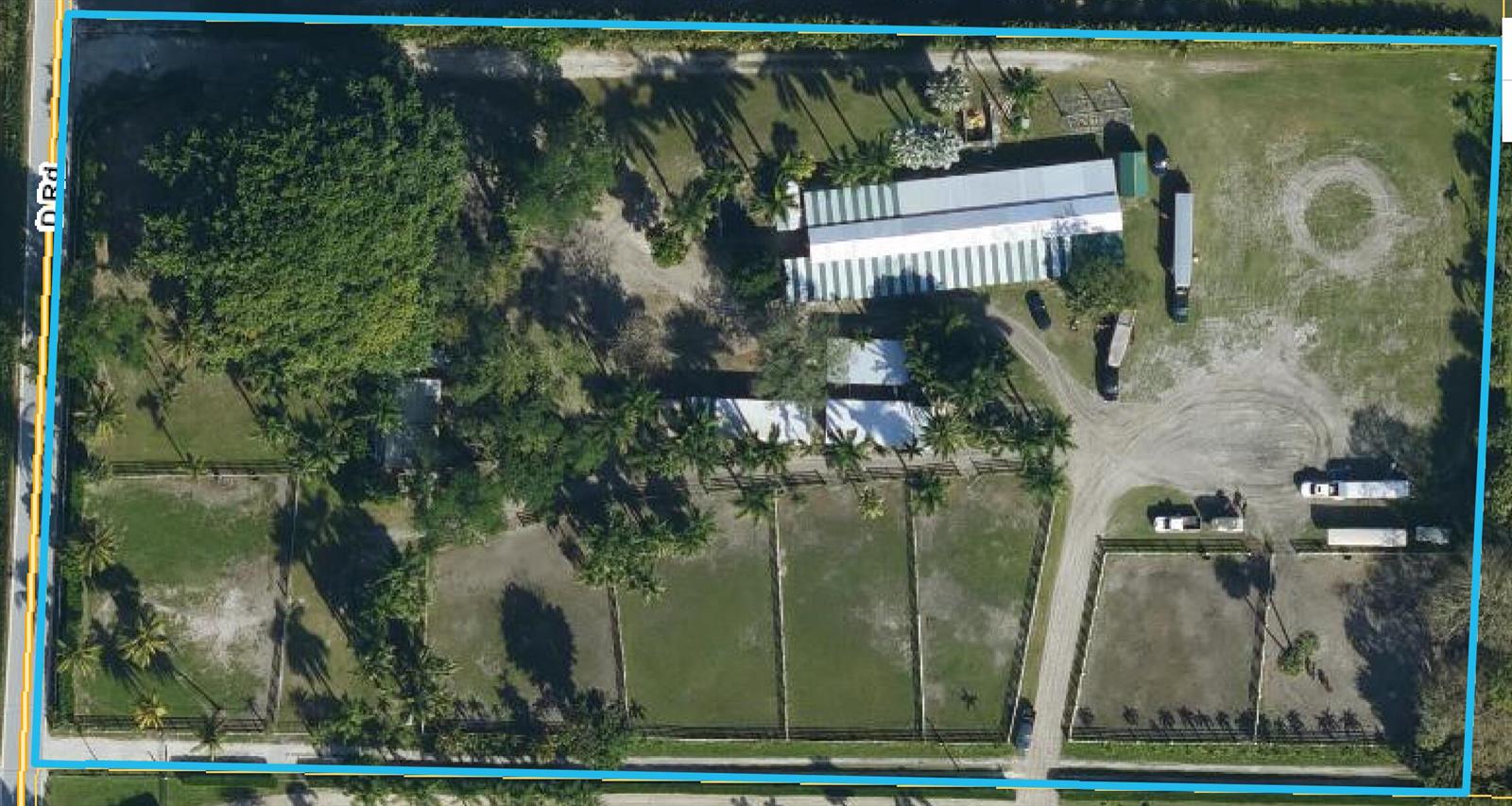 Aerial view of a rectangular property featuring a long building, multiple fenced paddocks, and trees — 1100 D Road, FL 33470, FL