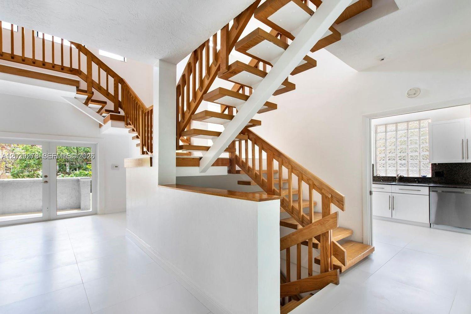 A white interior features a wooden staircase with railings and a nearby kitchen area — 2000 S Bayshore Dr # 58, Miami FL 33133, MIAMI, FL