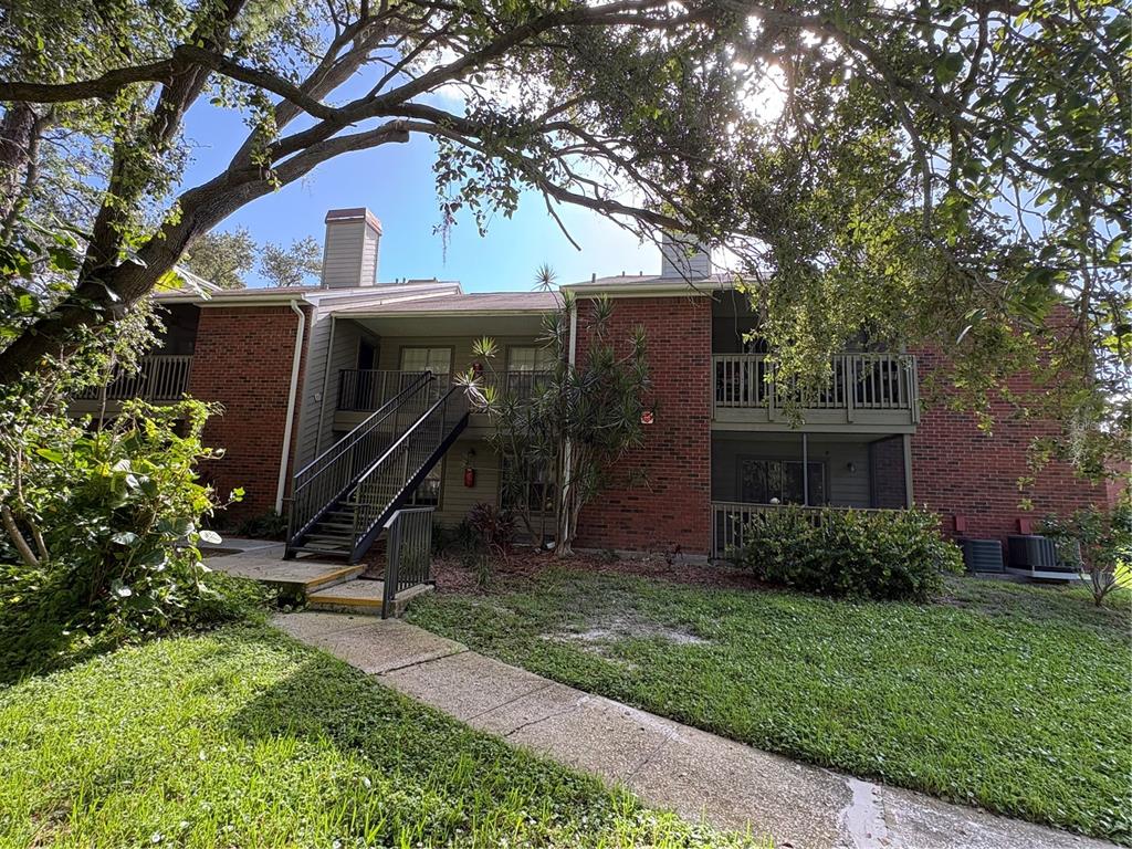 A two-story brick apartment building with exterior staircases and screened balconies under large oak trees — 9100 DR MARTIN LUTHER KING JR STREET N UNIT 1707, ST PETERSBURG, FL