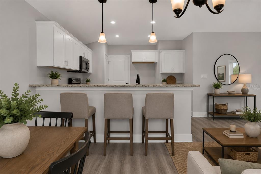 A kitchen with white cabinets and a breakfast bar overlooks a dining and living area — 4368 MERCEDES STREET, SEBRING, FL