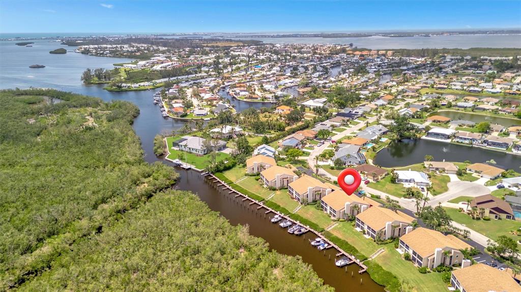 This aerial view shows waterfront condominiums with boat slips along a canal near a forest — 8710 54TH AVENUE W UNIT 8710, BRADENTON, FL