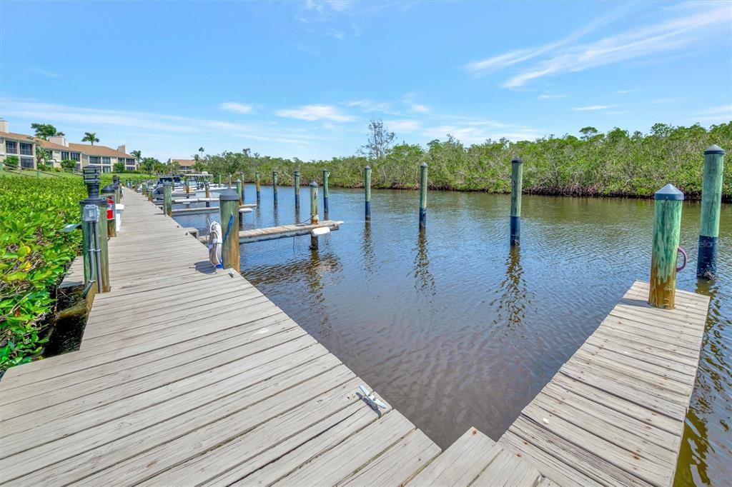 A wooden boat dock extends over a calm waterway lined with mangroves and distant buildings — 8710 54TH AVENUE W UNIT 8710, BRADENTON, FL