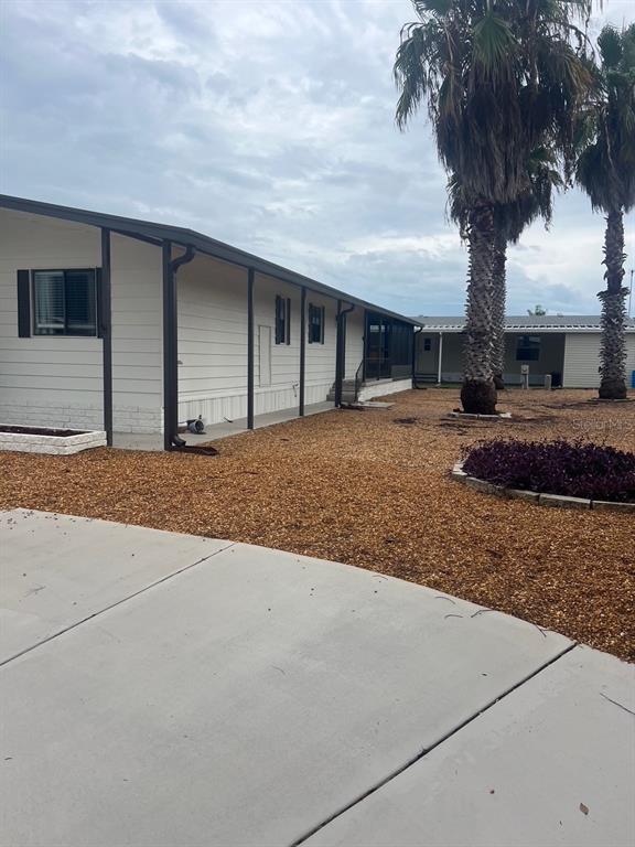 A light-colored mobile home with a covered porch sits next to palm trees and gravel — 12343 LARIAT WAY, HUDSON, FL