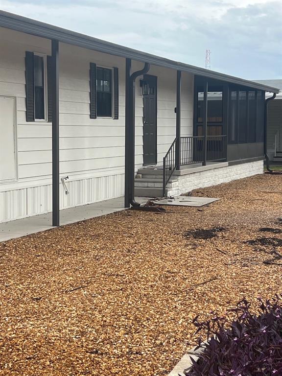 The exterior of a manufactured home features white siding, a screened porch, and gravel landscaping — 12343 LARIAT WAY, HUDSON, FL