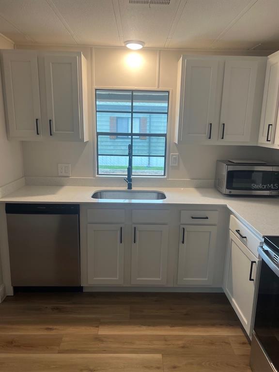 A kitchen with white cabinets, stainless steel appliances, a window, and light wood-look flooring — 12343 LARIAT WAY, HUDSON, FL