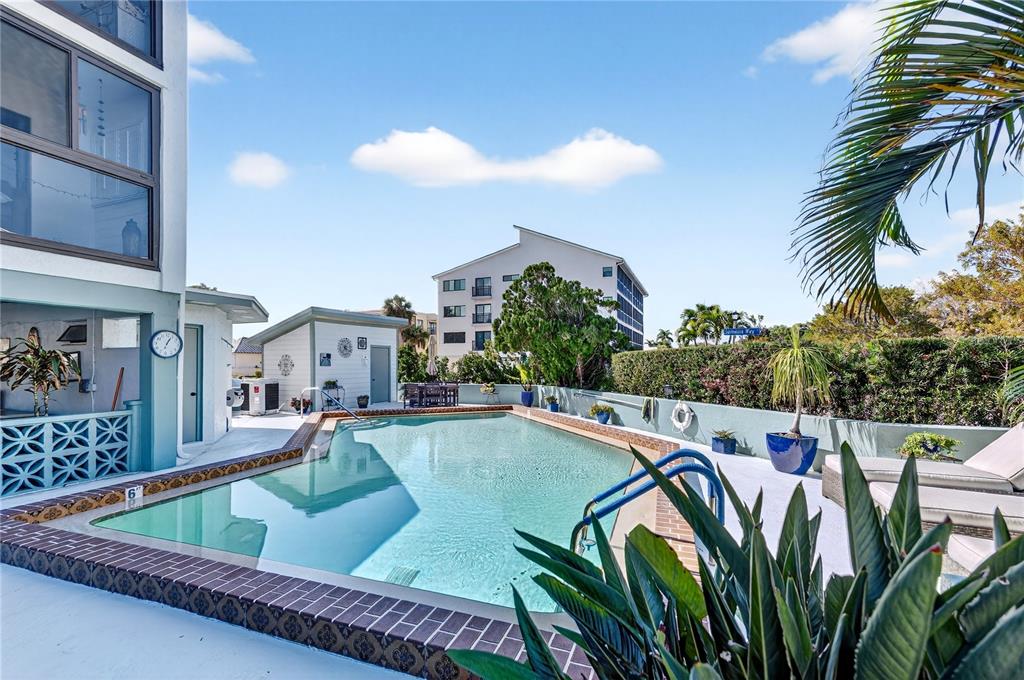 A swimming pool sits on a patio next to a multi-story building and small shed — 1765 JAMAICA WAY UNIT 101, PUNTA GORDA, FL