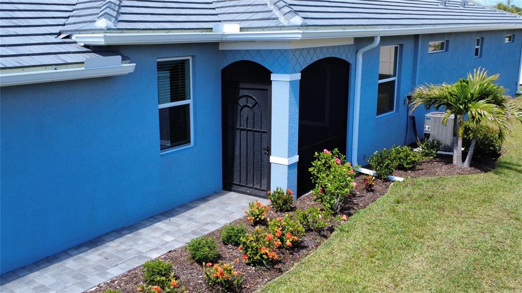 A blue house exterior features a screened entryway, a paved walkway, and a landscaped garden — 8125 SHORE LAKE DRIVE, ENGLEWOOD, FL
