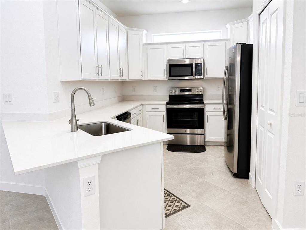 A kitchen with white cabinets, stainless steel appliances, and a white countertop peninsula — 8125 SHORE LAKE DRIVE, ENGLEWOOD, FL