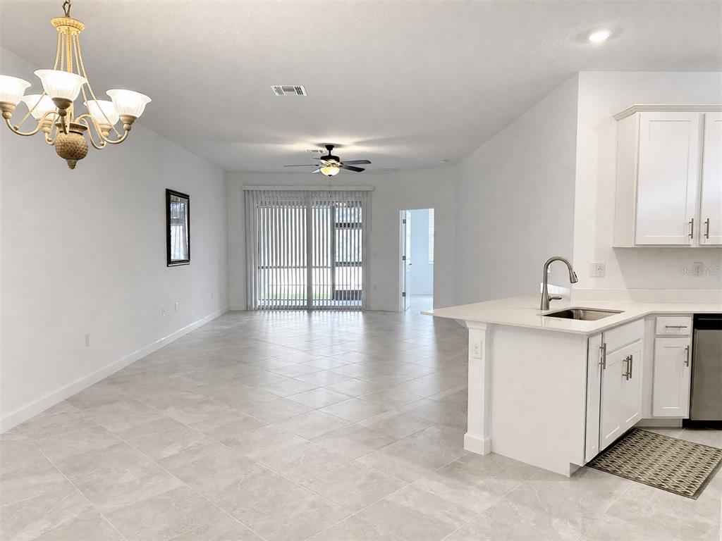 A bright open-concept kitchen and dining area features white cabinets, tile flooring, and sliding doors — 8125 SHORE LAKE DRIVE, ENGLEWOOD, FL