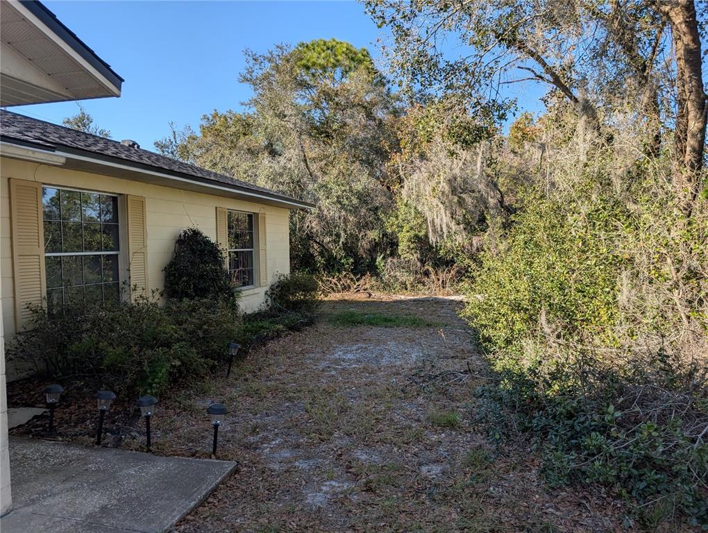 A side view of a house exterior with a sandy yard and surrounding trees — 24 S COURTLAND BOULEVARD, DELTONA, FL