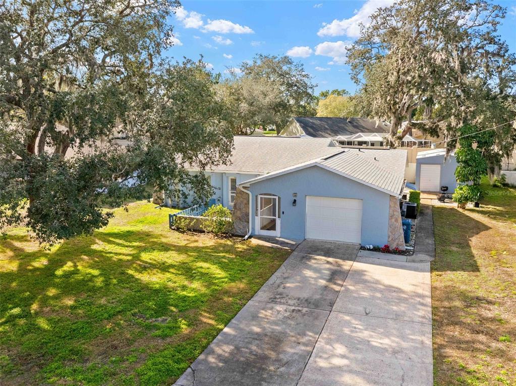 An exterior view of a light blue single-story house with a concrete driveway and trees — 2399 GALLAGHER AVENUE, SPRING HILL, FL